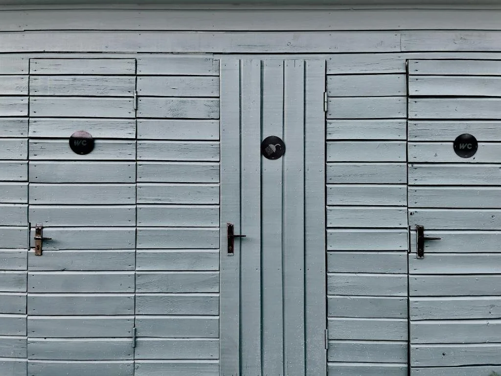 Wooden double doors painted light blue with circular black signs labeled 'WC', likely indicating restrooms.