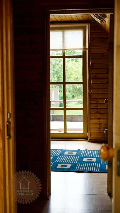 Looking through an open doorway into a room with a window and a blue rug on the wooden floor.