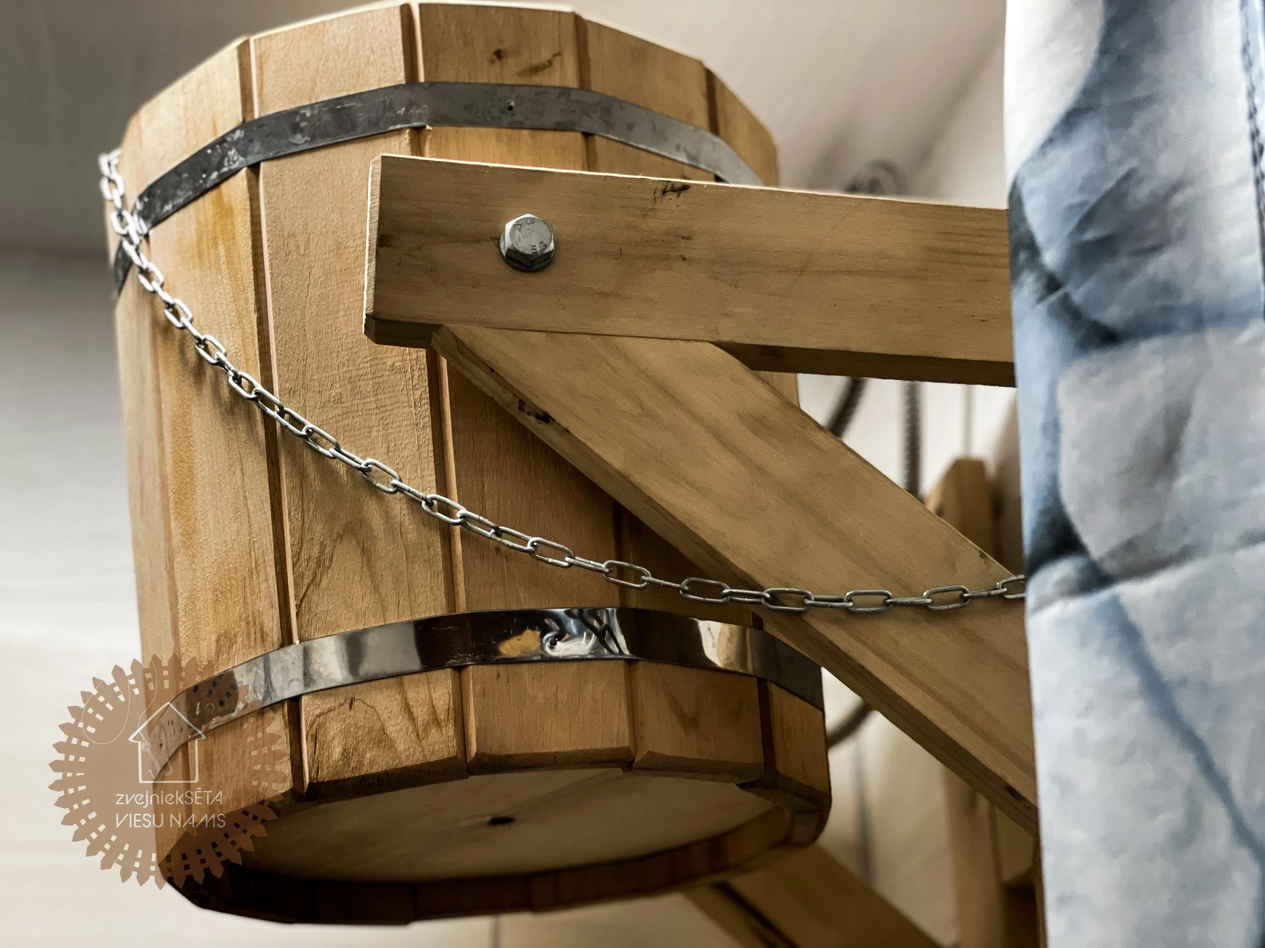 Close-up view of a wooden sauna heater with metal bands and a metal chain, seen from below.