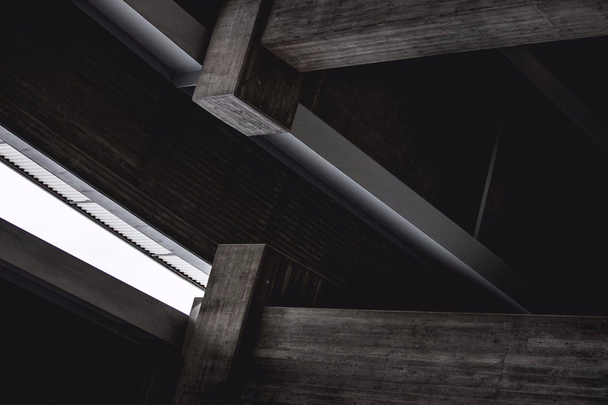 Interior of a modern building with concrete beams and dark walls, viewed from below.