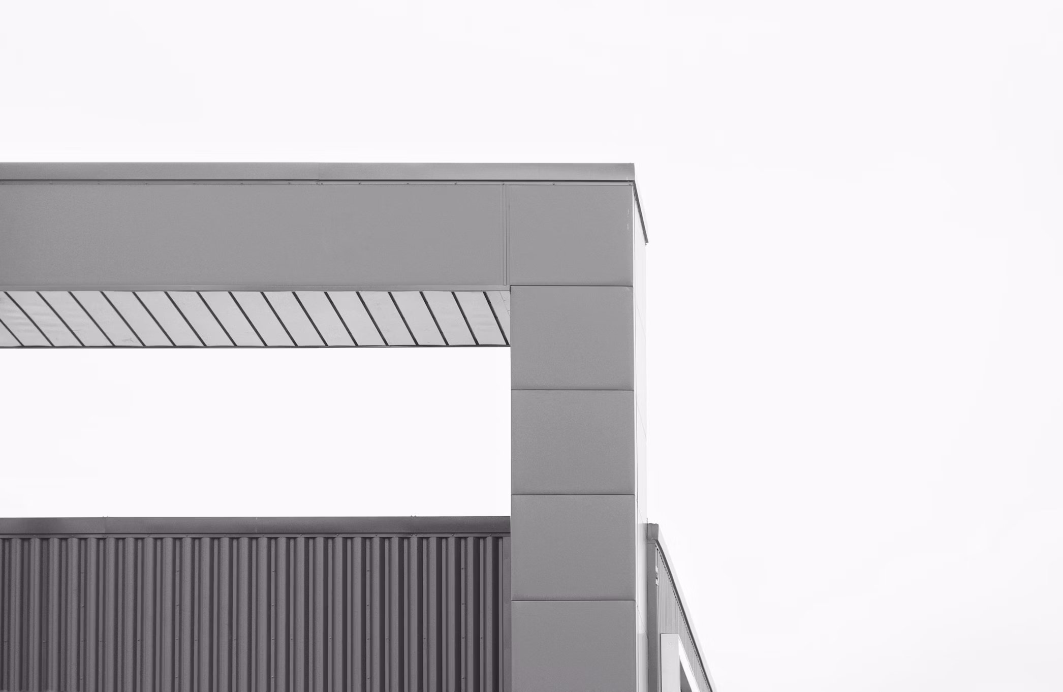 Close-up of modern gray building corner with metal panels and a slanted roof, against a clear sky.