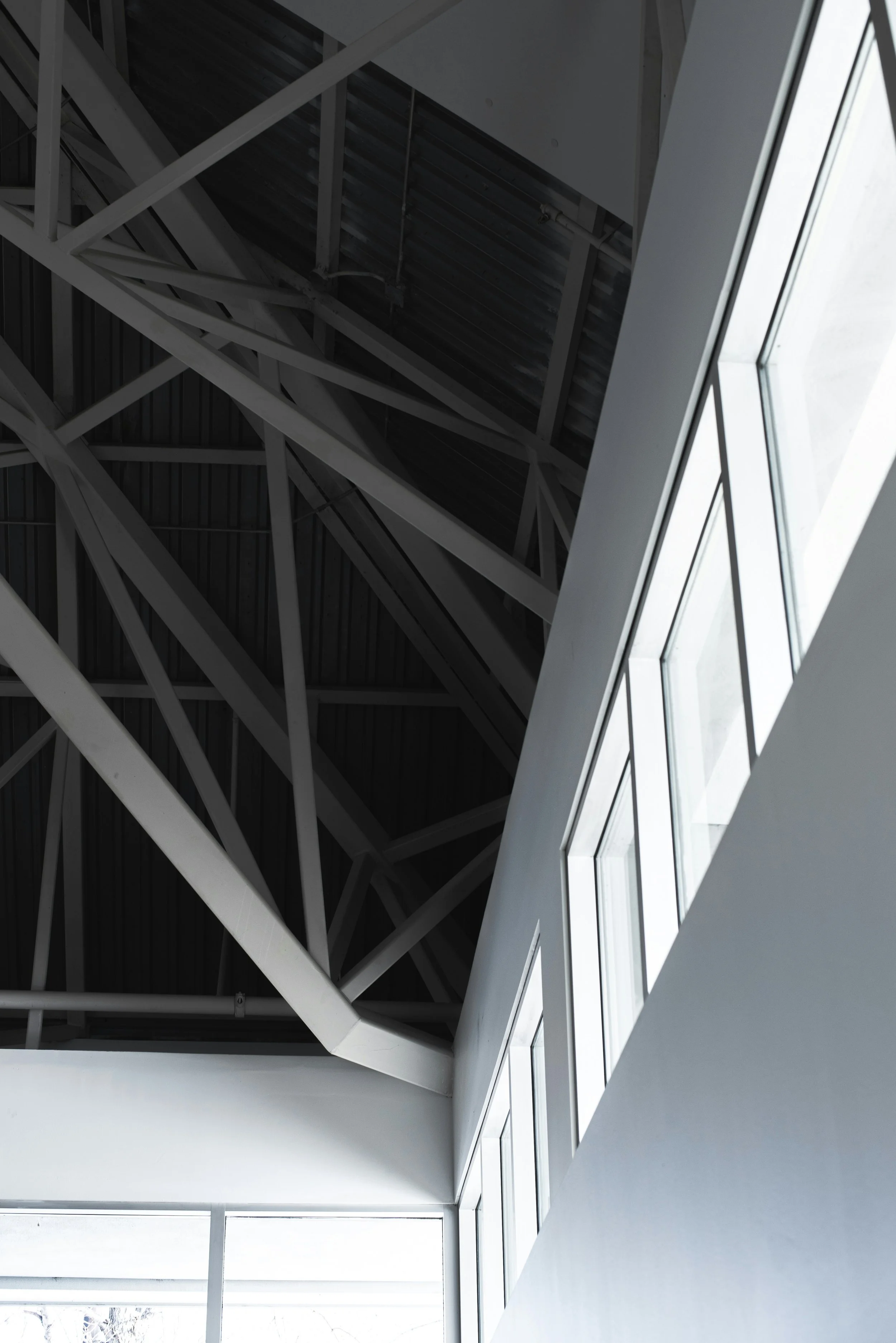 Interior view of a modern building with geometric ceiling structure made of metal beams and large windows letting in natural light.