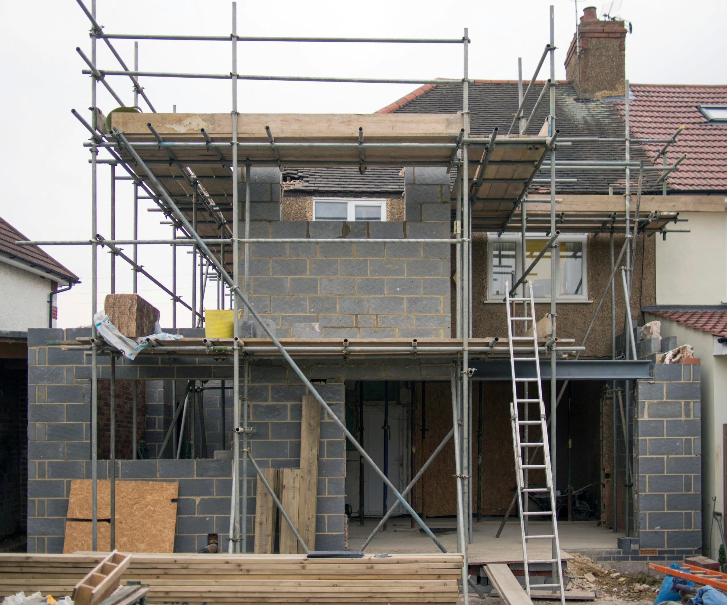 Construction site of a house with scaffolding, partially built brick walls, and building materials.