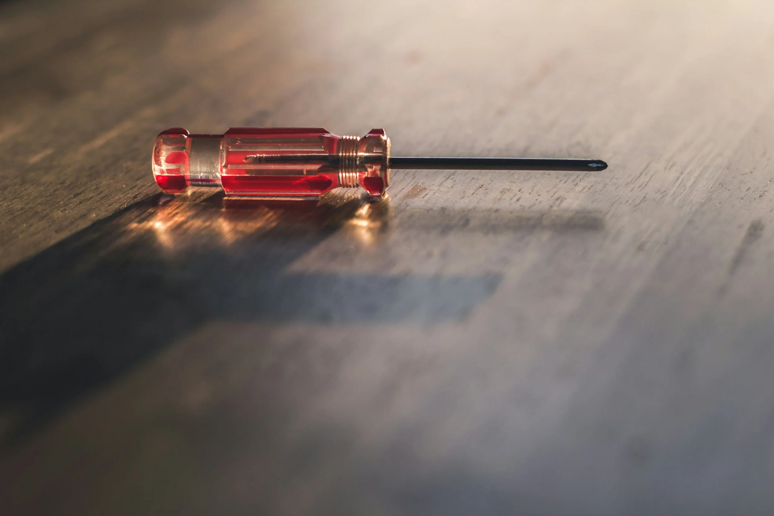 A red and transparent screwdriver lying on a wooden surface.