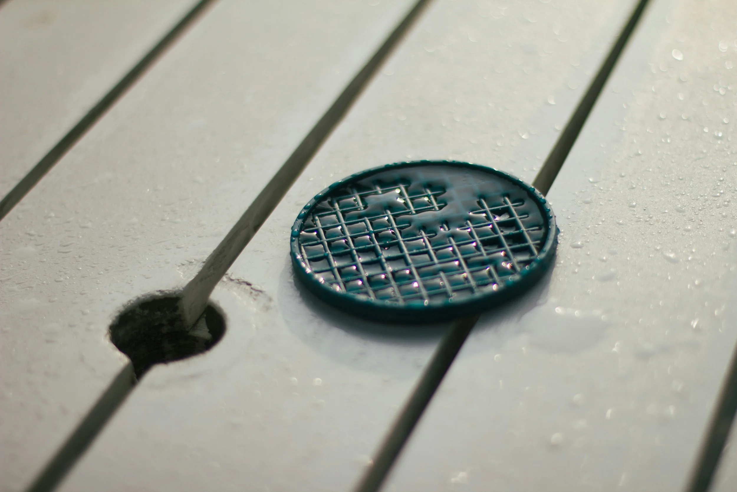 A tennis ball retriever basket on a white tennis court with water droplets, next to a hole in the court.