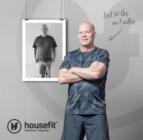 A man standing with arms crossed in front of a wall, smiling, with a before photo of himself in a frame behind him. The text on the wall notes he lost 50 pounds in 7 months. Housefit Personal Training logo is at the bottom.