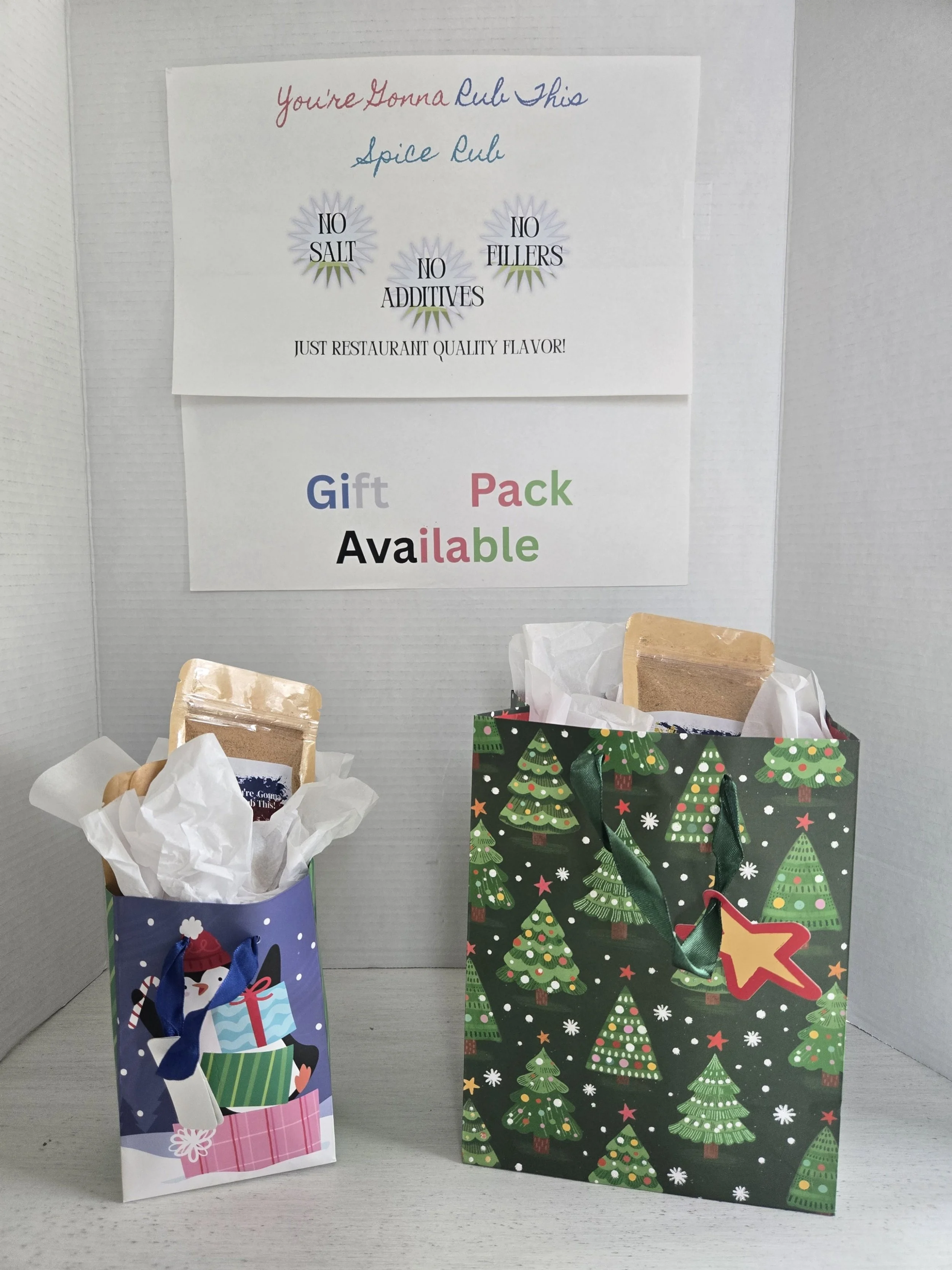 Two Christmas gift bags filled with tissue paper and wrapped items, placed on a white surface against a plain background with holiday signs and a Christmas-themed sign.