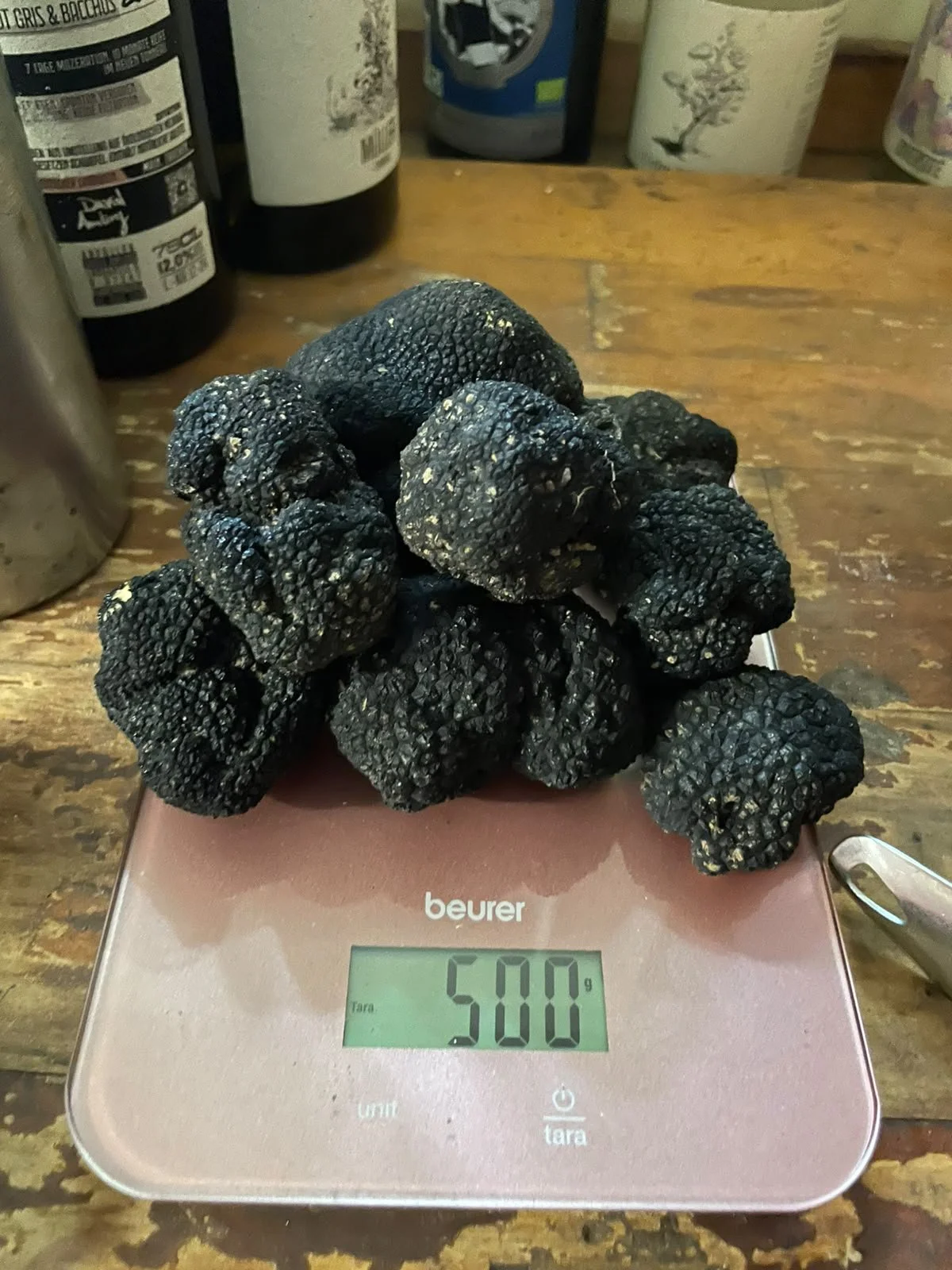 500 Gramm Trüffel liegen auf einer digitalen Küchenwaage. Im Hintergrund sieht man verschiedene Naturweine von David Amling.