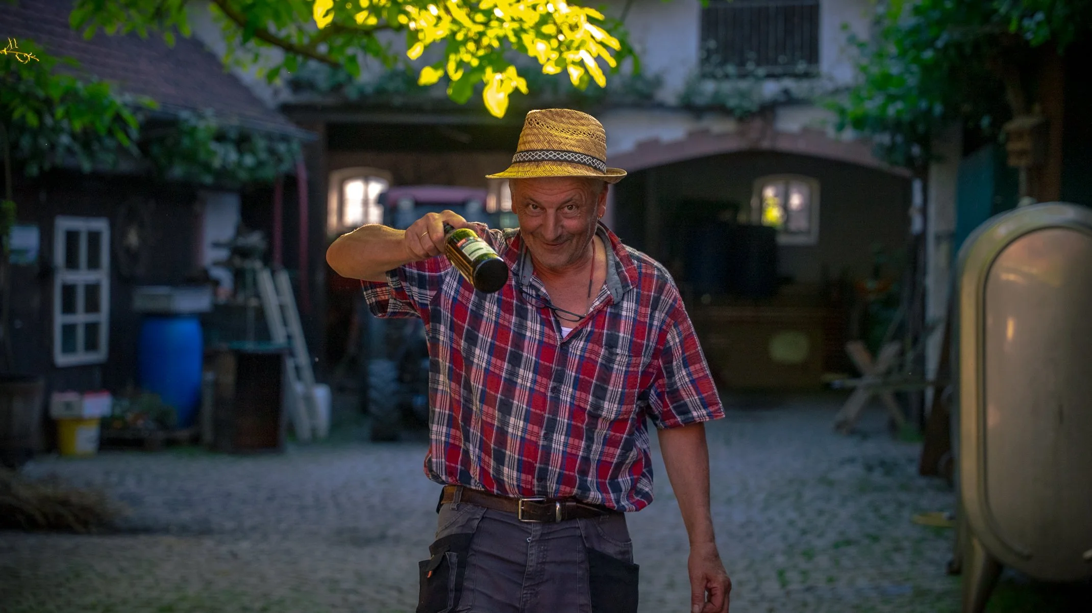 Winzermeister Dieter Amling steht im Hof von Weingut Amling und präsentiert Lachend eine Flasche Wein.