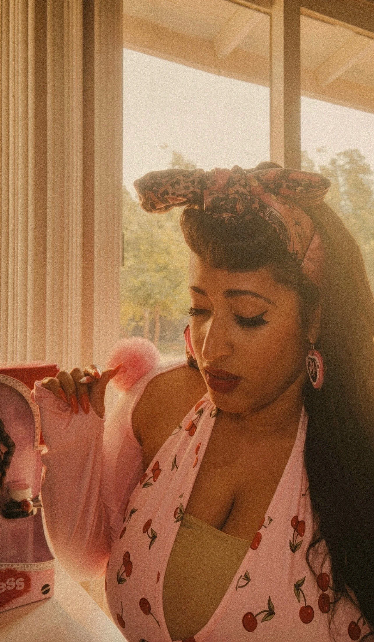 Erika Broussard, psychic advisor and intuitive guide, wearing a pink headscarf and cherry-patterned top, posed near a window with natural light in a vintage-inspired style.