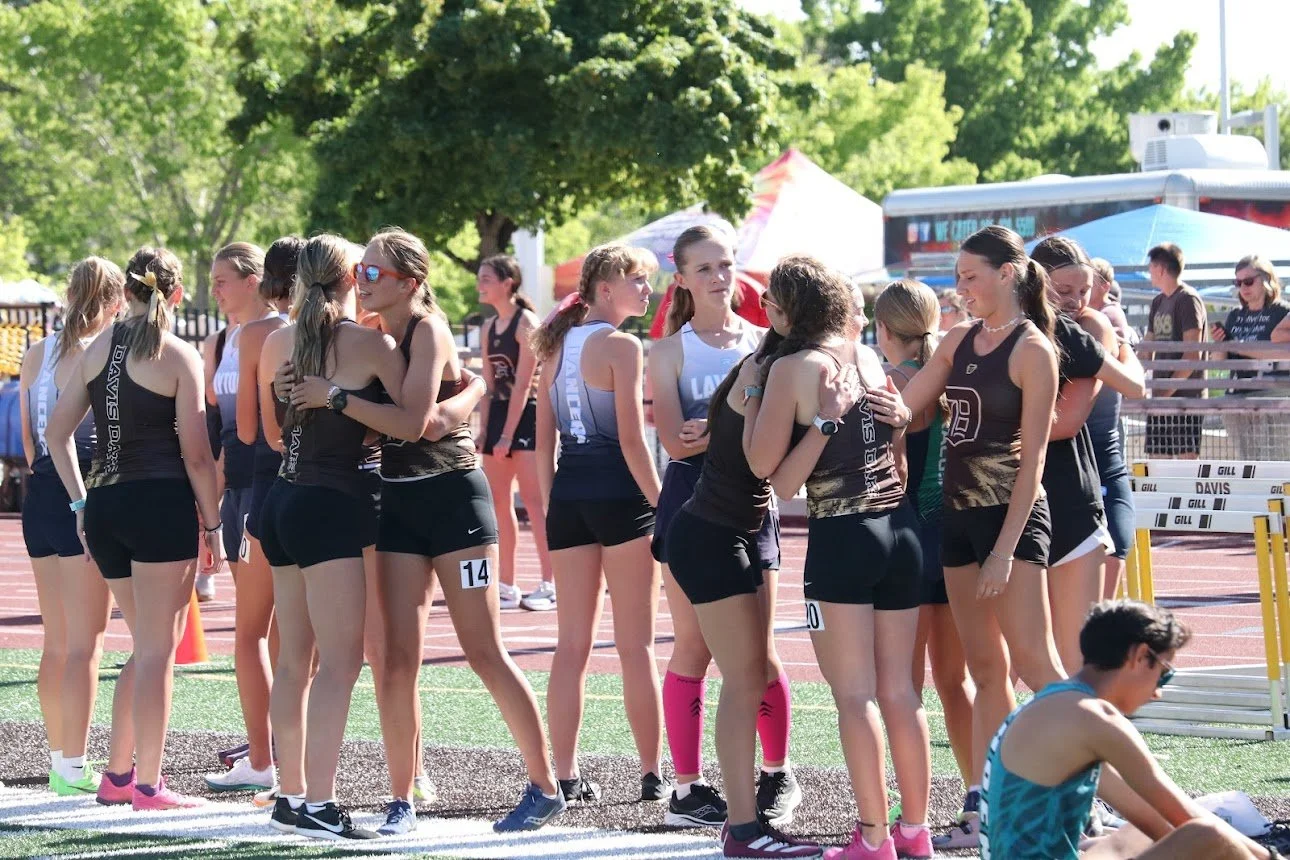 Track and field athletes hugging and greeting each other on a running track during a sunny day at a sports event.