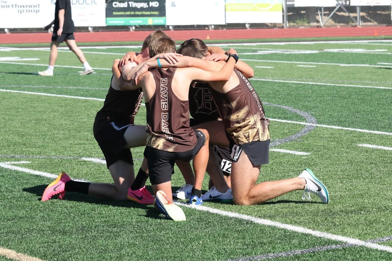 Group of young athletes, wearing matching brown and black sportswear, kneeling in prayer before a race.