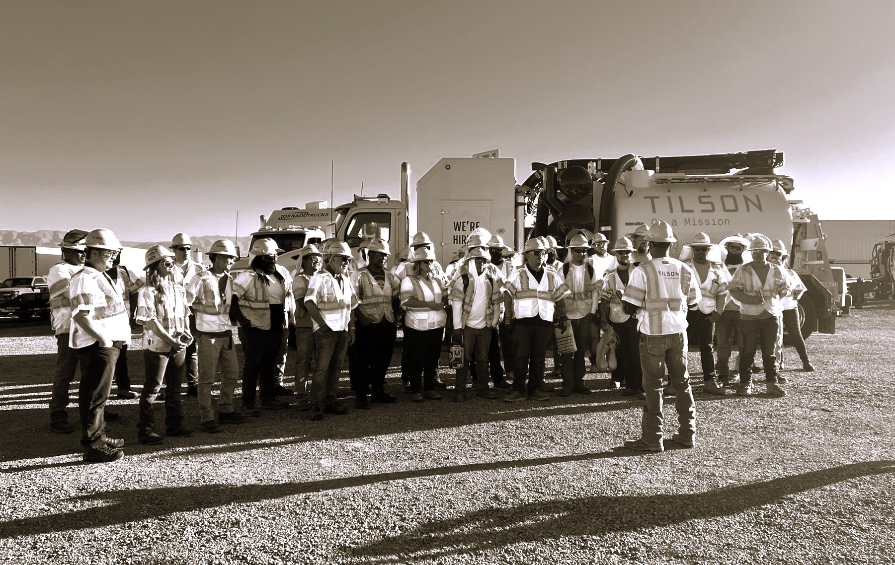 Group of construction workers in a field meeting while wearing hi-vis vests and hard hats