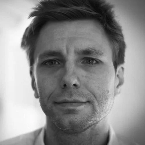 Mustavalkoinen kuva miesstä, joka katsoo kameraan, lyhyt hius ja neutraali ilme.