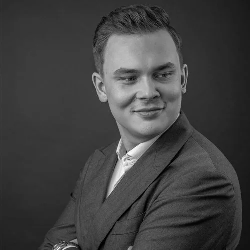 Mies pukeutuneena puku ja valkoinen paita, hymyilee ja katsoo oikealle, mustavalkoinen kuva.