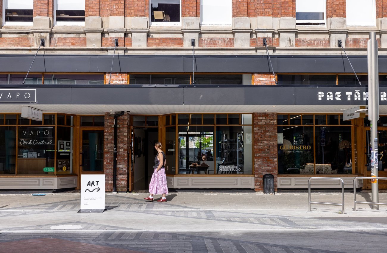 Woman walking along a street looking into a shop front labelled Art Gallery & Design Studio