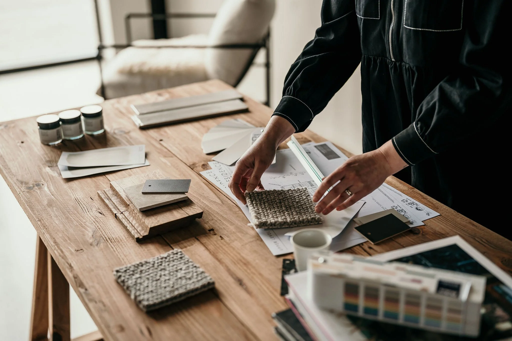 Person examining fabric samples on a wooden table with various design materials and color swatches.