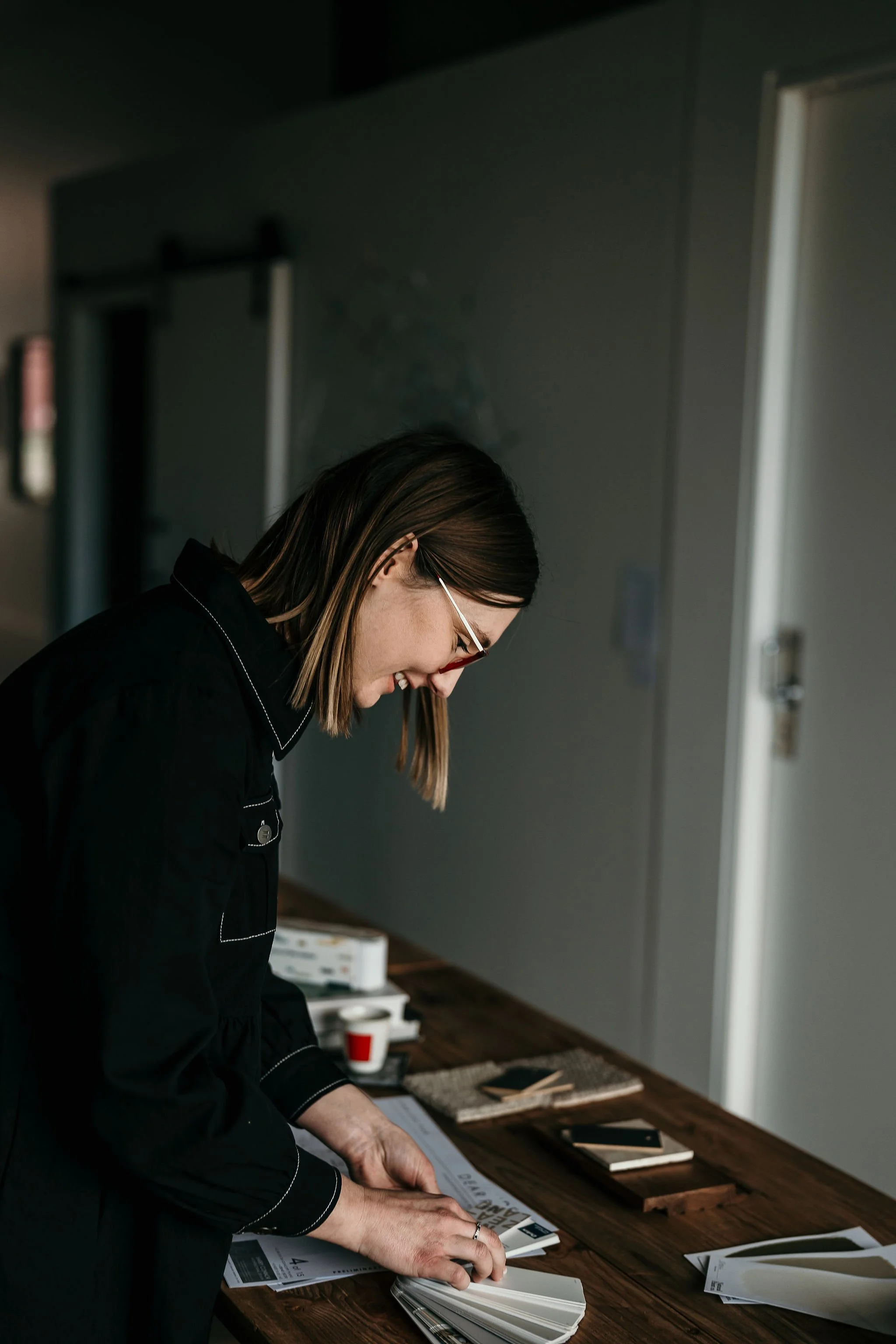 Woman with glasses leaning over a table with design materials, color swatches, and papers.