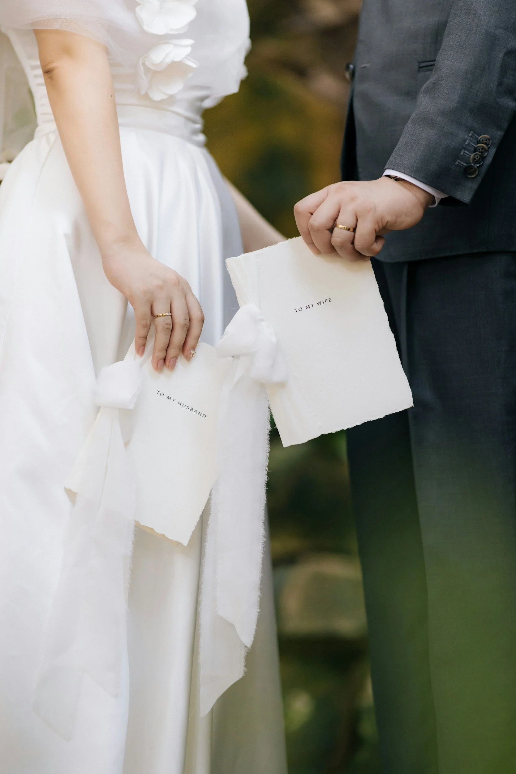 Close-up of a bride and groom holding decorative gifts with 'To My Wife' and 'To My Husband' text, during a wedding ceremony.