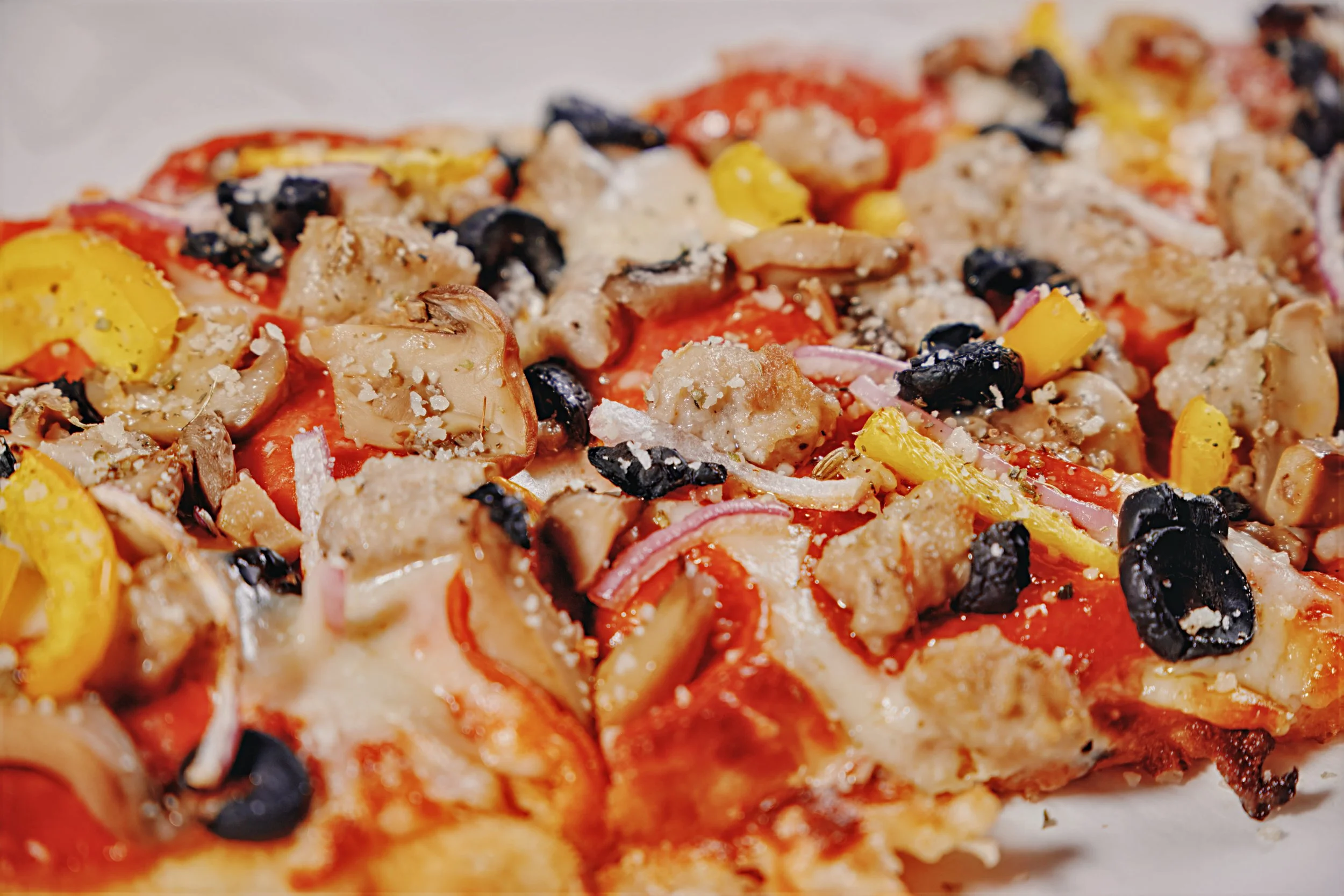 Close-up of a pizza with various toppings including black olives, yellow bell peppers, mushrooms, tomatoes, onions, and melted cheese.