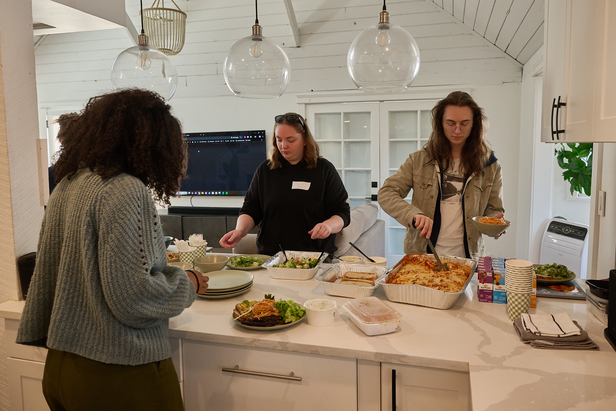 People serving themselves food from a buffet in a bright kitchen.
