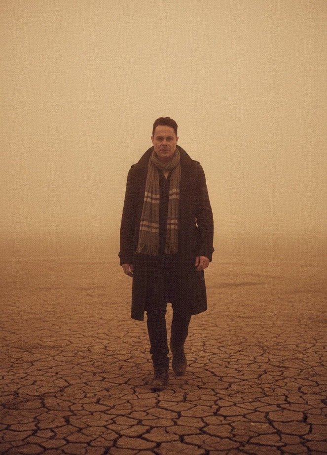 A man walking on cracked, dry desert ground with a hazy, orange sky in the background. Time Traveler walking out from a time portal .  Jorge Heredia