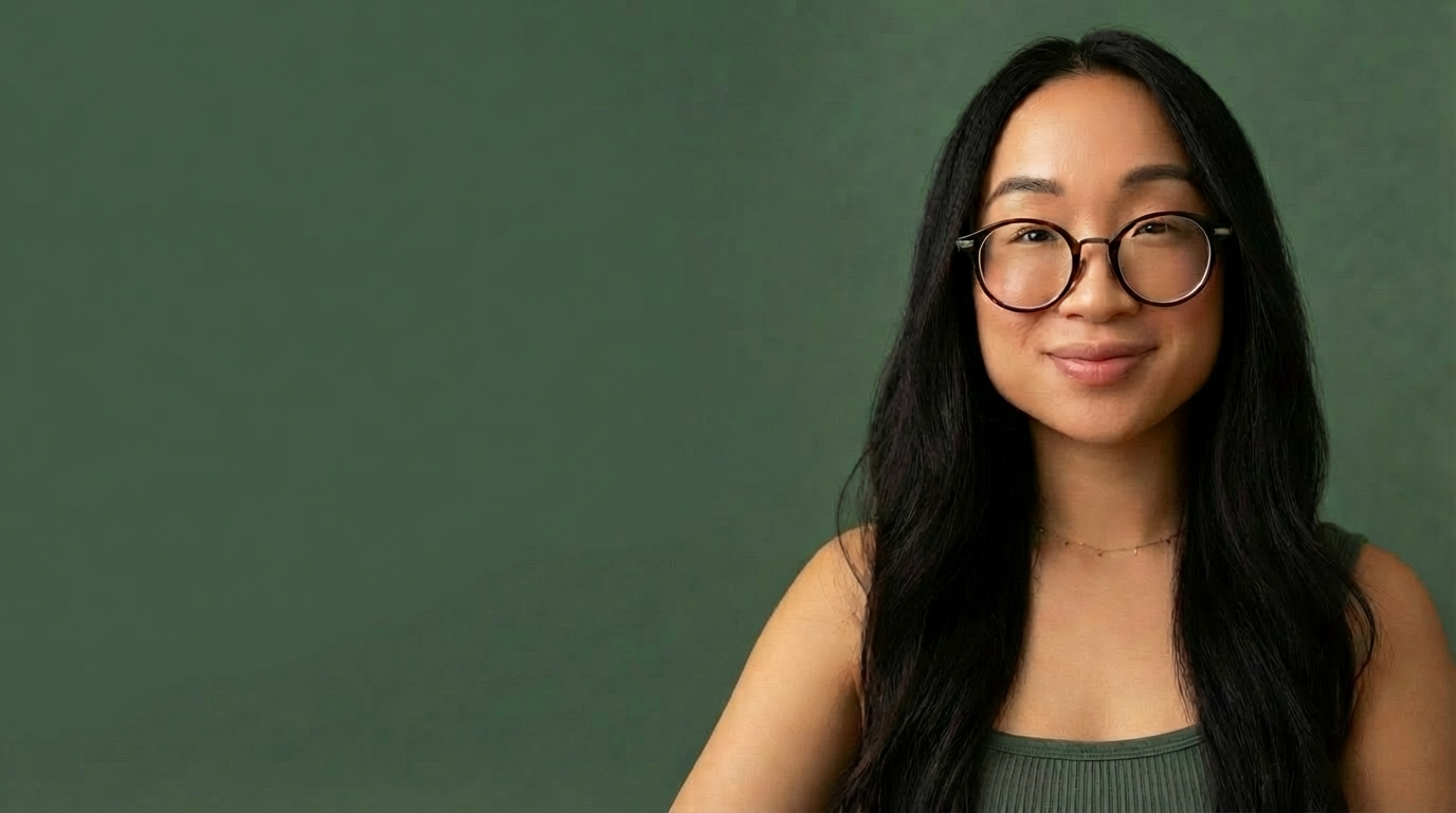 A woman with long black hair, glasses, and a subtle smile, standing against a green background.