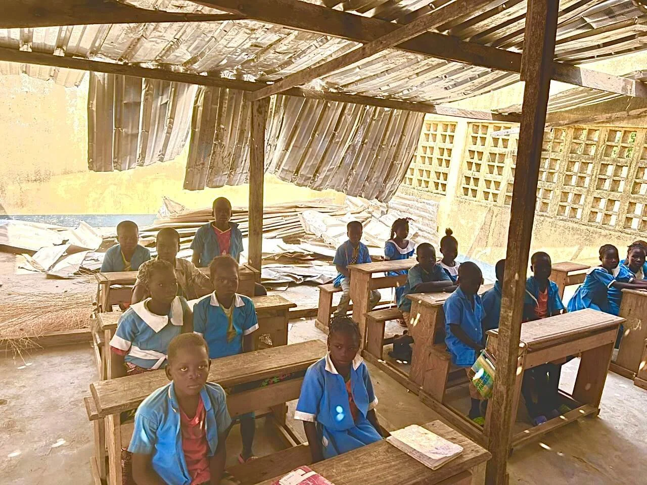 Schoolchildren in blue uniforms sitting at wooden desks inside a Central African classroom.