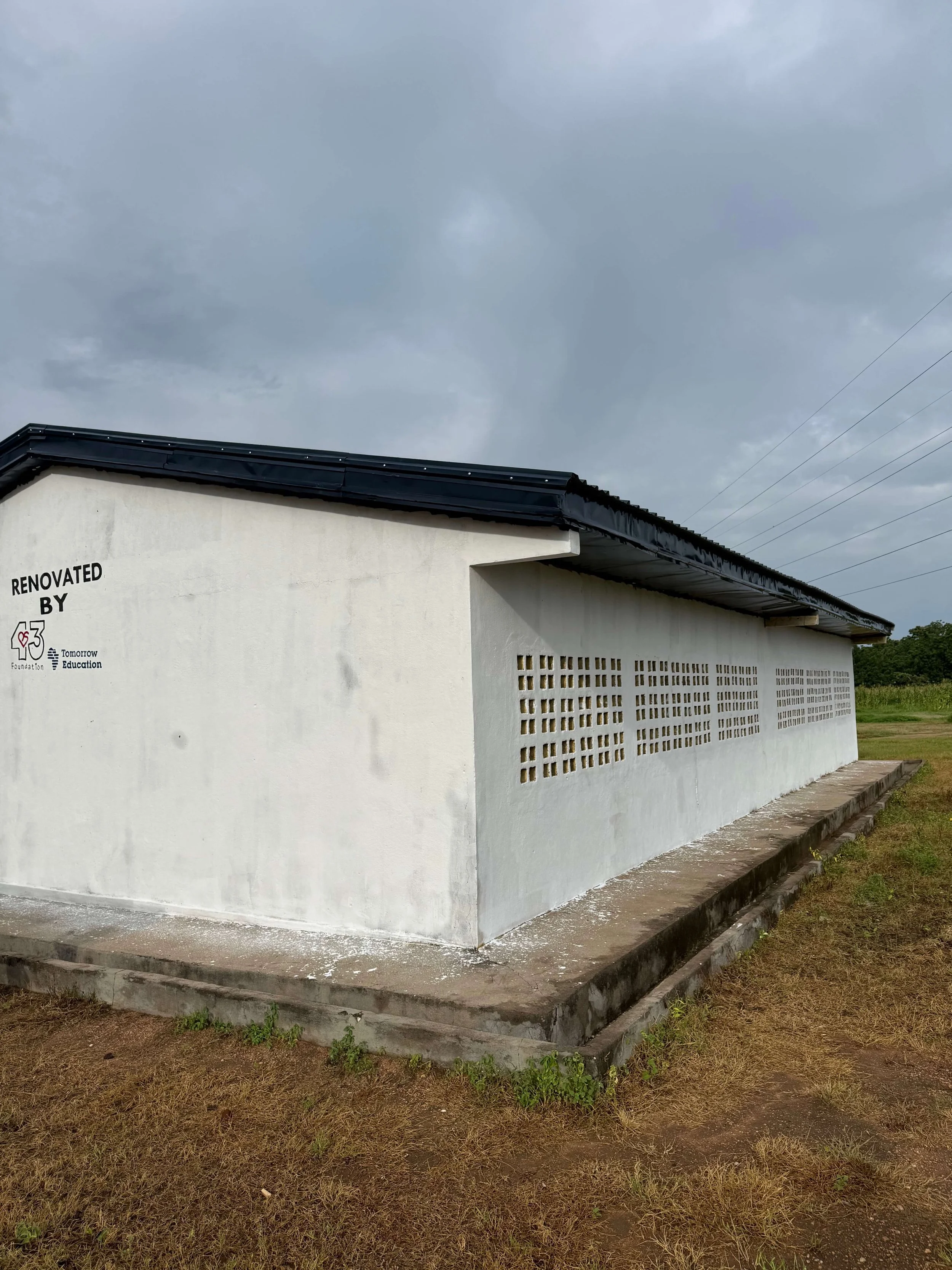 Renovated white concrete building with ventilation blocks, black roof, and foundation logos under a cloudy sky