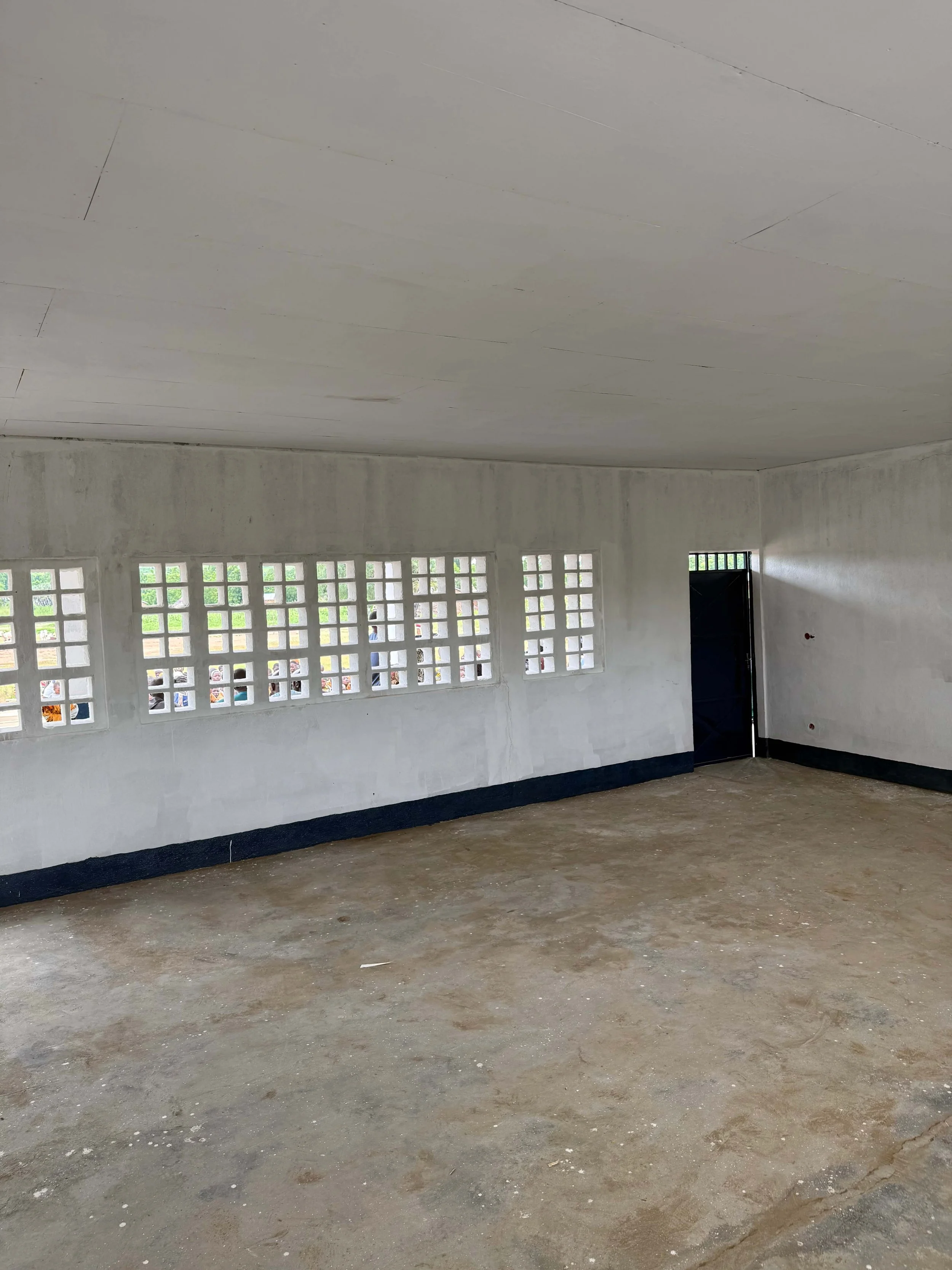Unfurnished concrete interior with white walls, patterned ventilation windows, a black door, and floor.