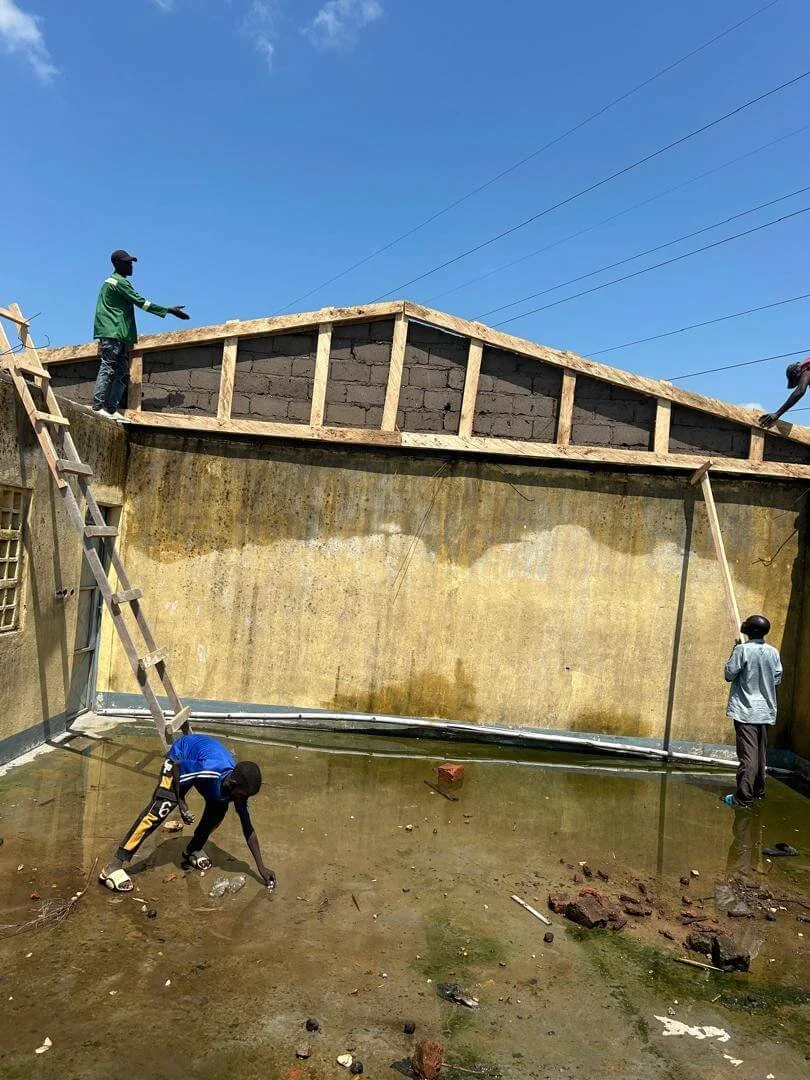 Workers cleaning a flooded concrete courtyard beneath a partially constructed roof on a sunny day