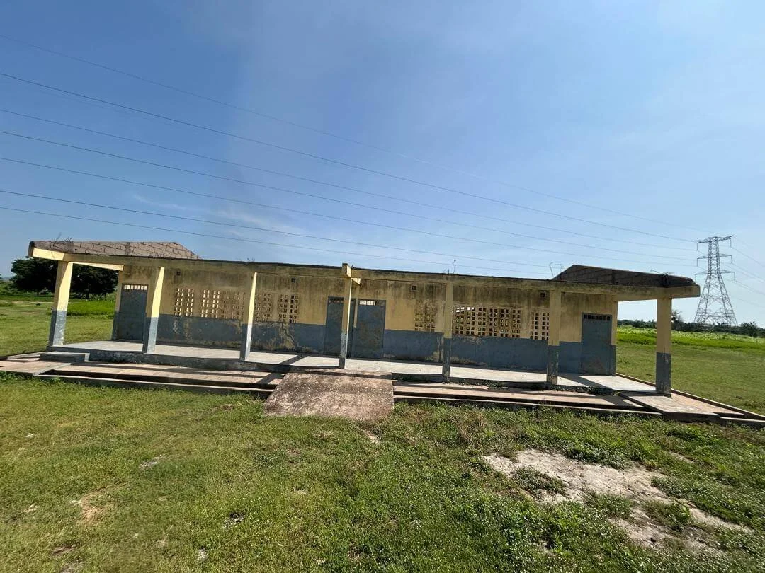 Old concrete school building with covered walkways in a grassy field beneath power lines