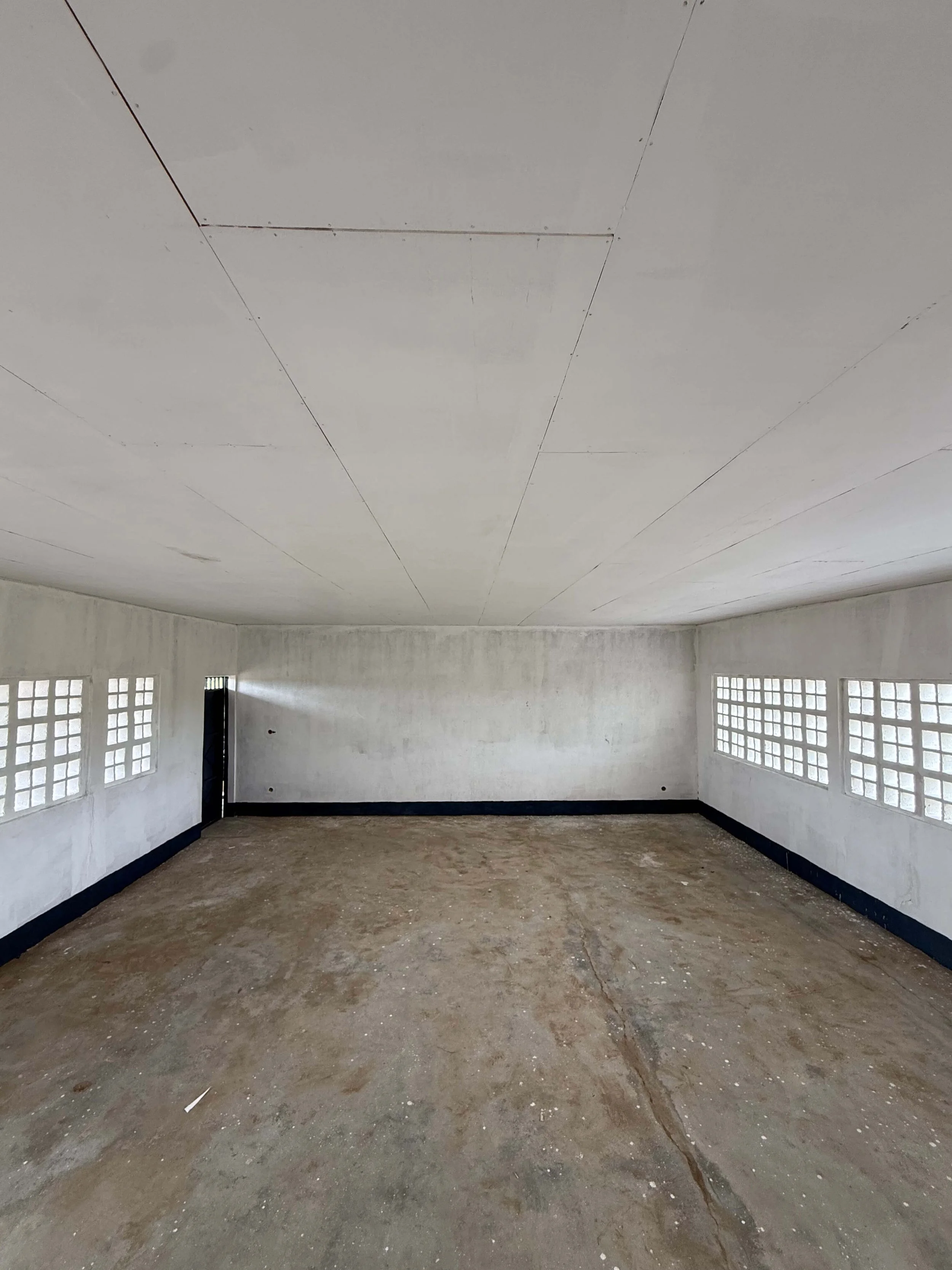 Empty unfinished concrete room with white walls, glass-block windows, black trim, and floor