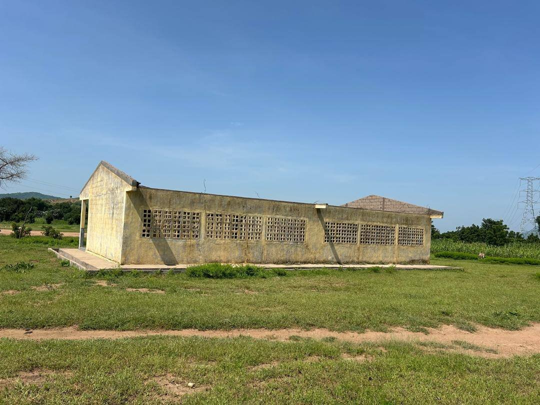 Weathered concrete building with patterned ventilation blocks in a grassy rural field under a clear blue sky