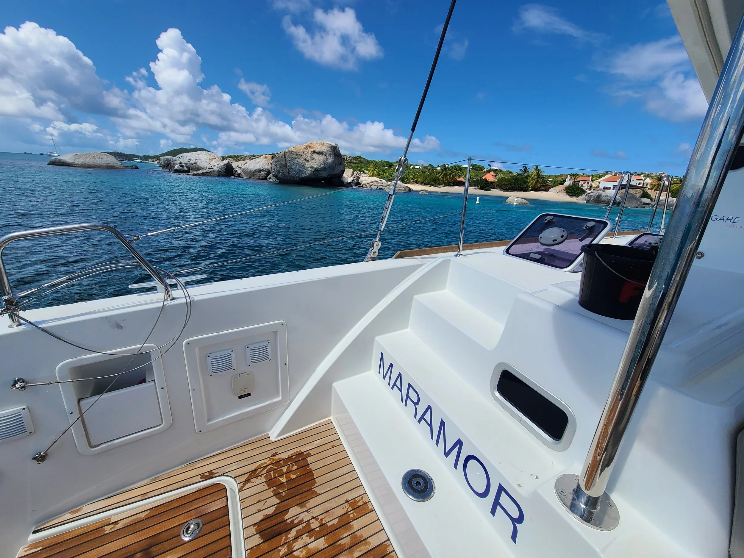 View from a boat showing blue ocean water, rocky islands, and a distant shoreline with trees and buildings under a partly cloudy sky.