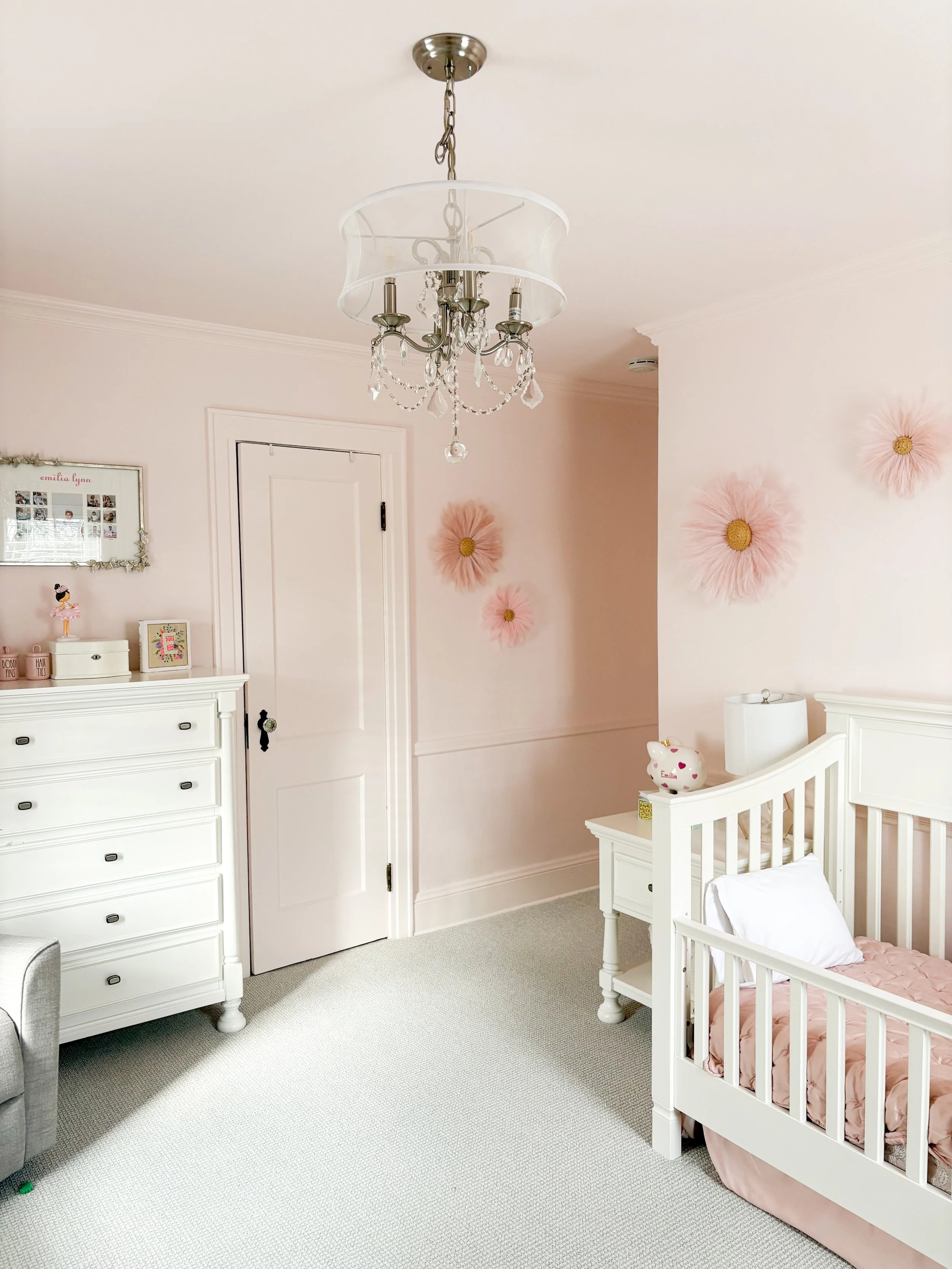 A decorated children's bedroom with pink flower wall decorations, white furniture, and a chandelier