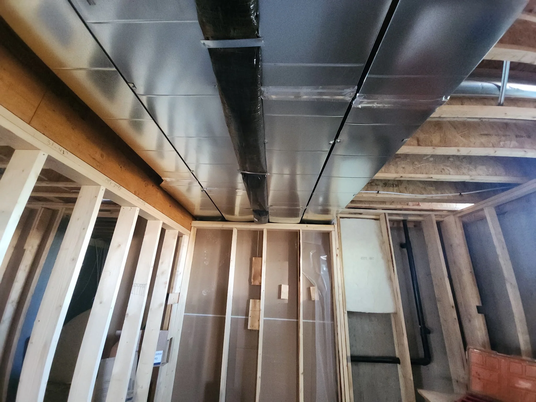 Construction site with wooden framing, a metal duct, and black piping.