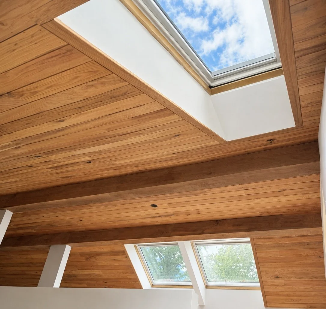 Room with wooden ceiling and skylight windows showing blue sky and clouds