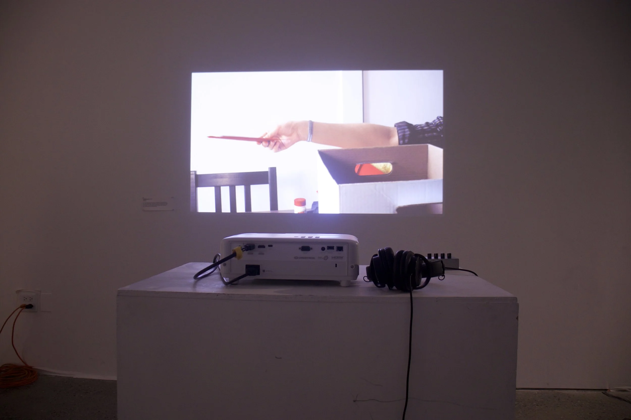 Projection of a person pointing with a red object, seen through a rectangular opening on a wall in a presentation setting.