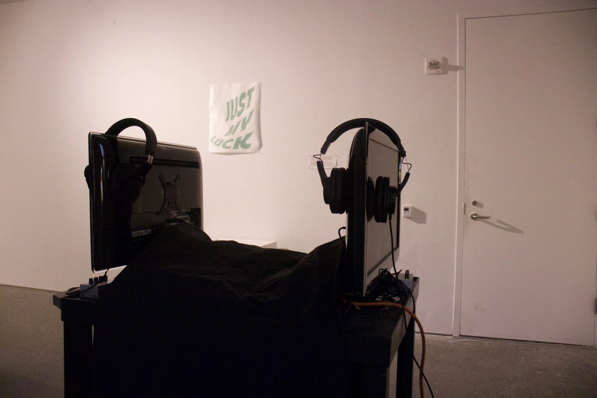 A room with a computer setup, headphones hanging on the side, a banner with the words 'JUST MY LUCK' on the wall, and a closed door in the background.