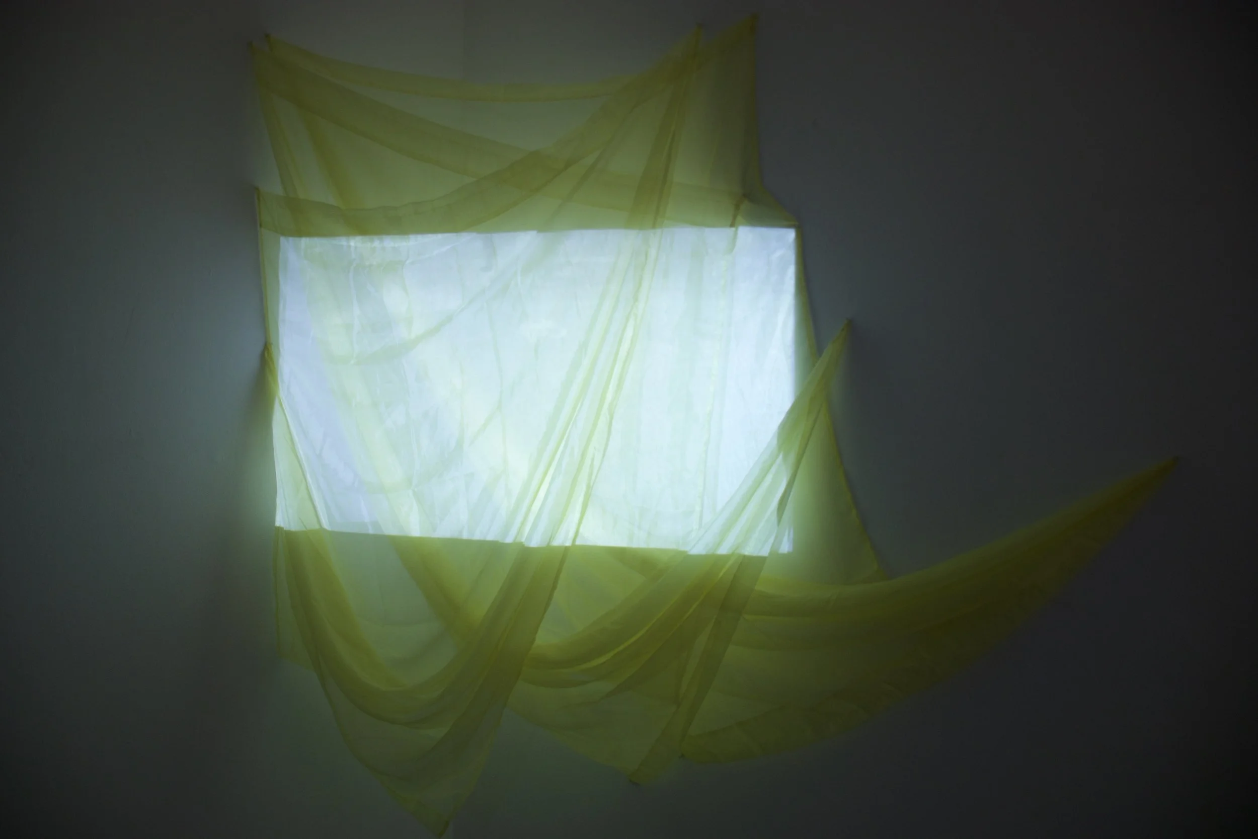 Yellow translucent fabric draped on a white surface with light shining through, creating a glowing effect.