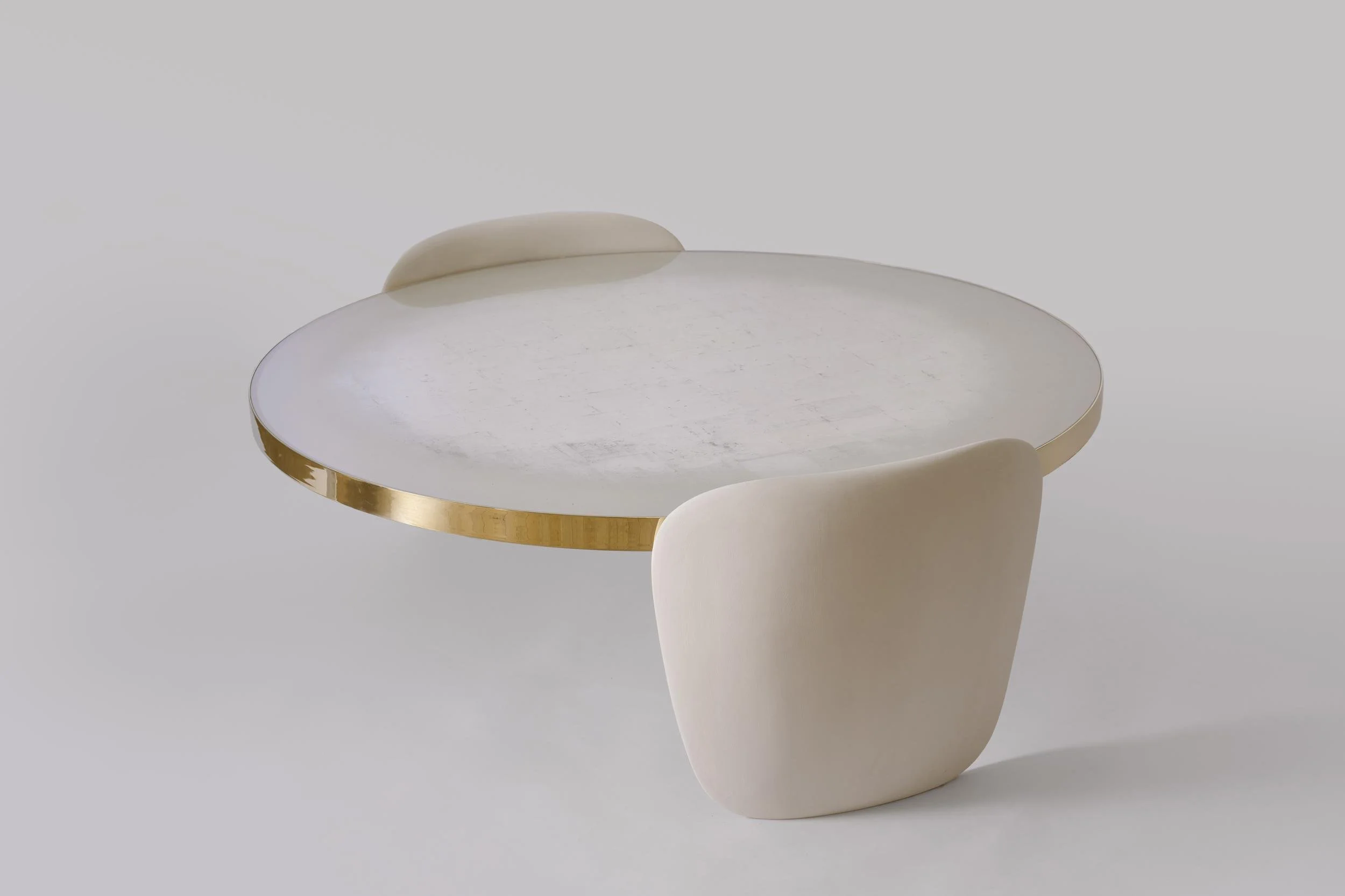 Modern round table with a white marble top and gold metallic trim, paired with two beige upholstered chairs with rounded backs.