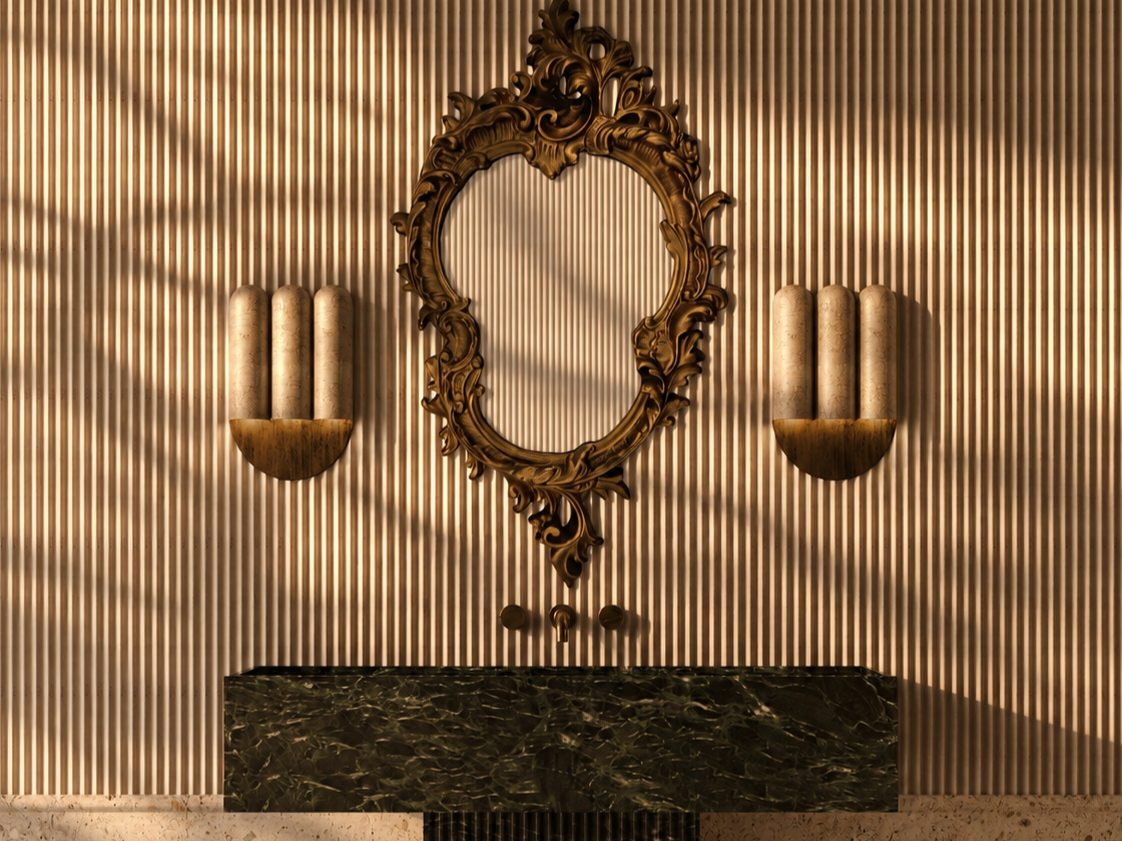 A decorative wall with vertical ridges featuring an ornate gold-framed mirror, gold wall sconces with candles, and a black marble sink below.