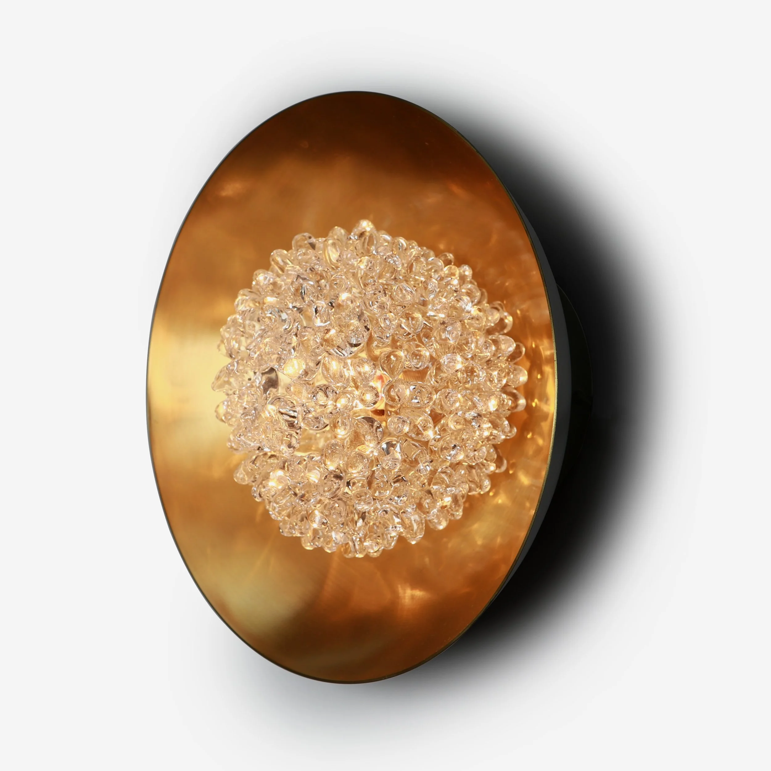 Close-up of a modern wall-mounted light fixture with a round black frame, a reflective gold interior, and a central cluster of small glass beads that diffuse the light.