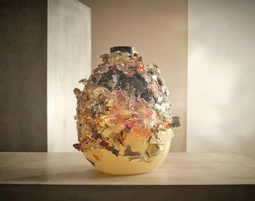 Ceramic vase with a textured, layered, metallic-colored glaze on a wooden surface, set against a simple background.