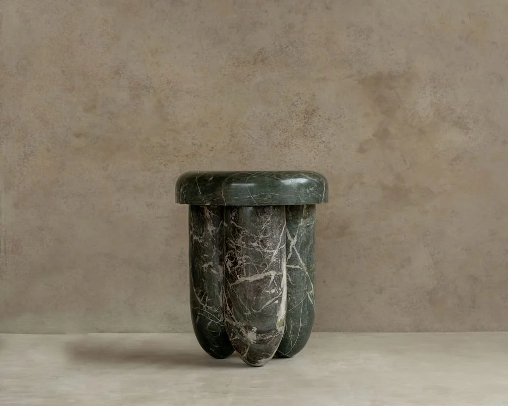 Green marble stool with a rounded top and three rounded legs against a beige wall.
