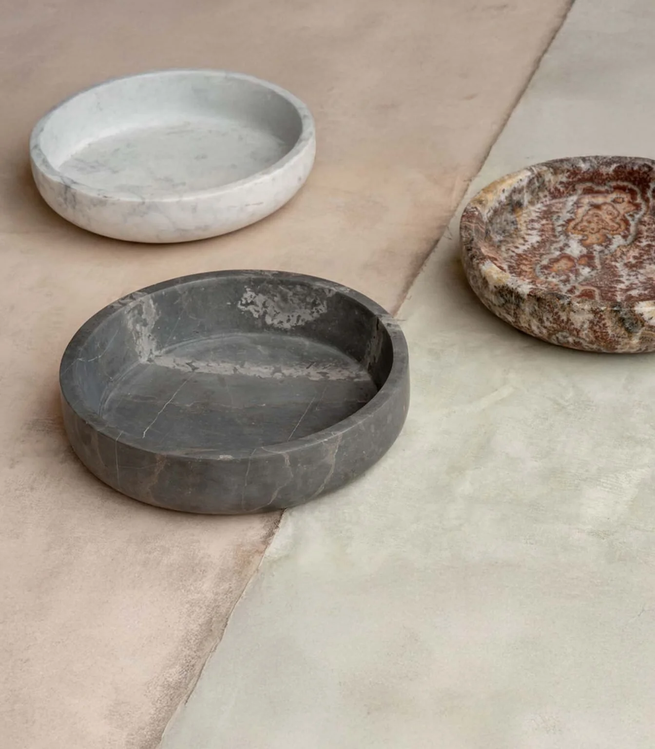 Three round stone bowls placed on a tiled surface with mixed colors of beige and cream.