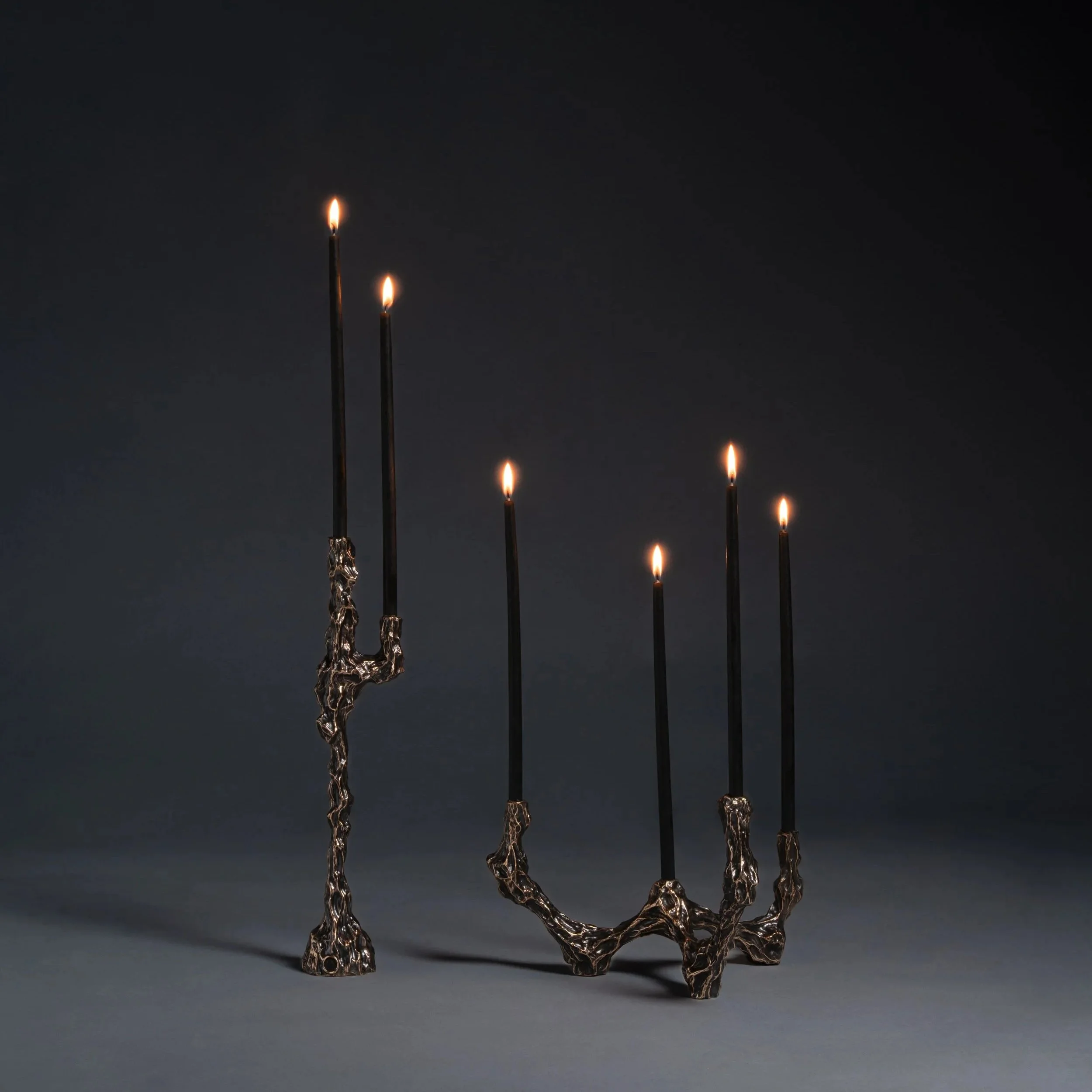 Contemporary black candles with melting wax in an artistic metal holder on a dark background.