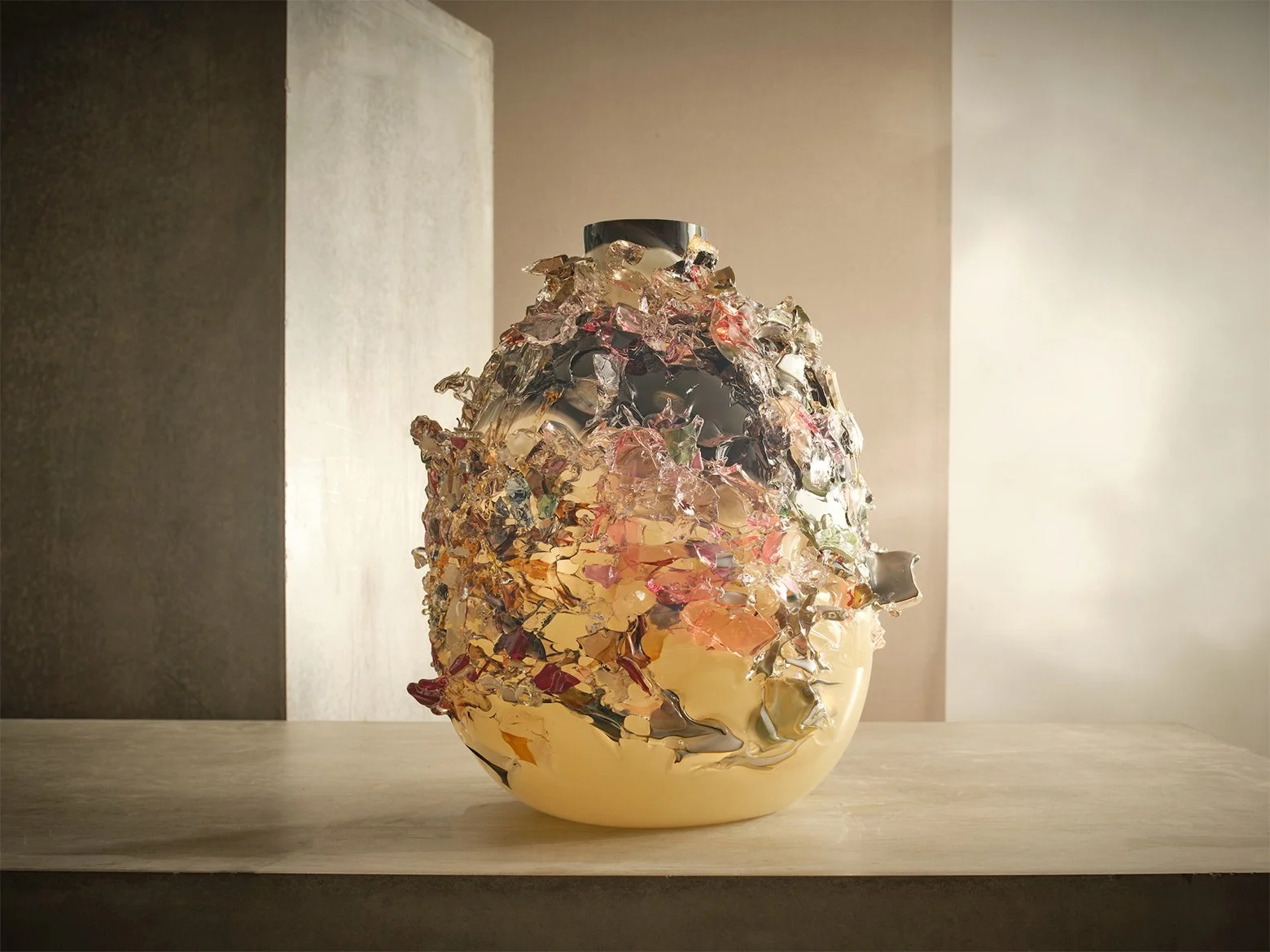 Decorative glass vase with a multicolored, textured surface placed on a light wooden surface with a plain background.