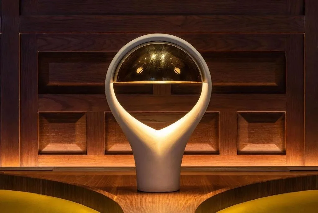 Decorative object with a white base and a reflective sphere on top placed on a wooden surface, with a wooden panel background.